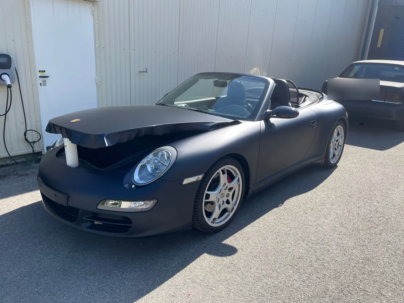 Porsche 911 cabriolet en PPF noir mat, capot à demi posé révélant la peinture brillante d'origine